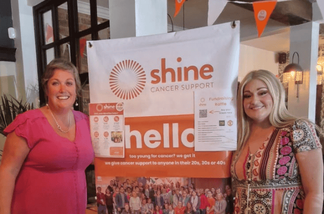 Two ladies from our Manchester Network in front of some Rise & Shine bunting and posters, and a pull up banner about Shine Cancer Support.